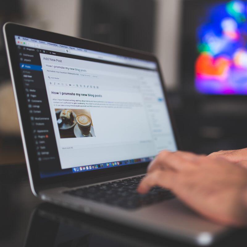 Ein WordPress Blogger hat ein Apple Macbook auf einem schwarzen Tisch stehen und schreibt einen Blog-Beitrag über Kaffee und Kuchen