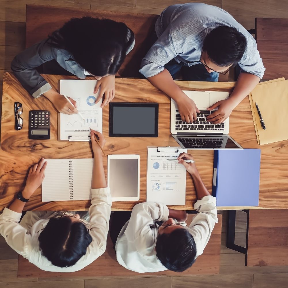 Draufsicht von einem Meeting-Team an einem Tisch mit verschiedenen Test-Geräten und Checklisten und 4 Personen in einer Besprechung